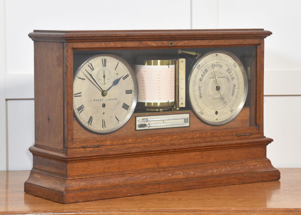 A glazed oak-cased antique weather station featuring a clock dial on the left, an aneroid barometer on the right, and a central paper drum barograph with an integrated thermometer. View V