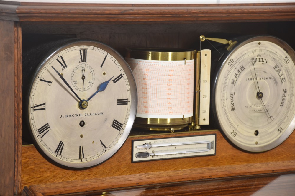 A glazed oak-cased antique weather station featuring a clock dial on the left, an aneroid barometer on the right, and a central paper drum barograph with an integrated thermometer. View VII