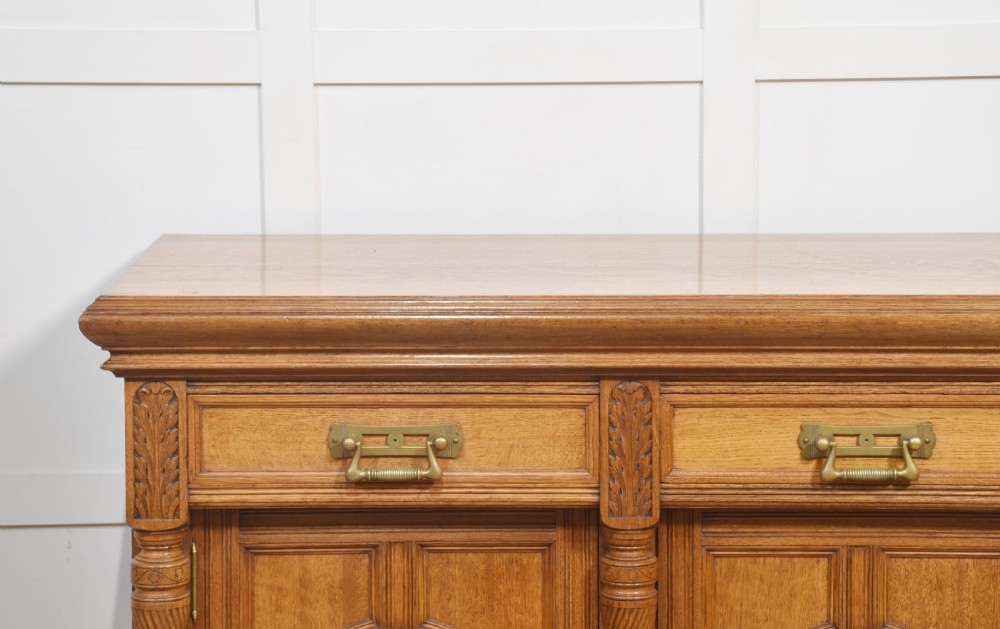 A carved oak two-door sideboard featuring two drawers with brass handles, central rosette carvings on the cupboard doors, and turned columns. View II