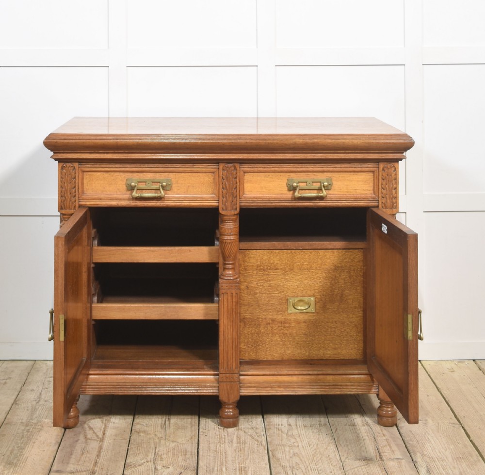 A carved oak two-door sideboard featuring two drawers with brass handles, central rosette carvings on the cupboard doors, and turned columns. View III