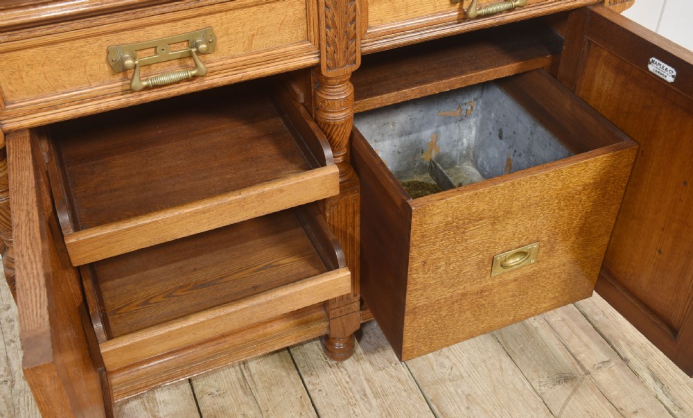 A carved oak two-door sideboard featuring two drawers with brass handles, central rosette carvings on the cupboard doors, and turned columns. View V