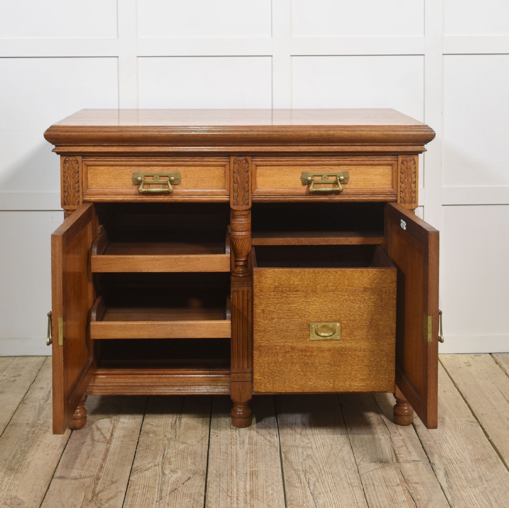 A carved oak two-door sideboard featuring two drawers with brass handles, central rosette carvings on the cupboard doors, and turned columns. View IX