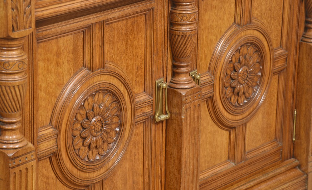 A carved oak two-door sideboard featuring two drawers with brass handles, central rosette carvings on the cupboard doors, and turned columns. View X