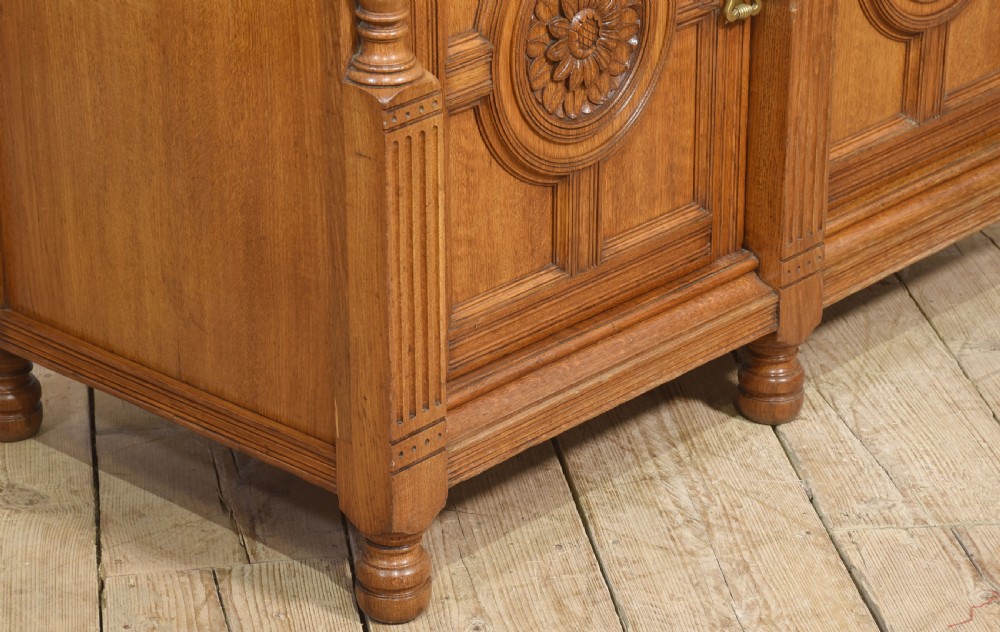 A carved oak two-door sideboard featuring two drawers with brass handles, central rosette carvings on the cupboard doors, and turned columns. View XI