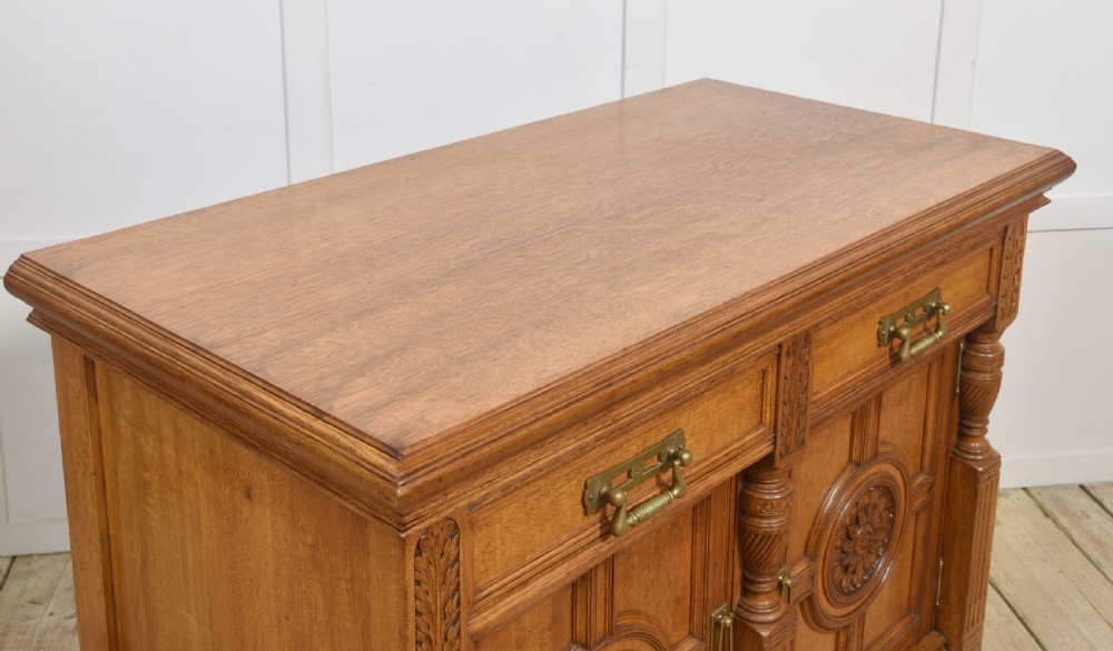 A carved oak two-door sideboard featuring two drawers with brass handles, central rosette carvings on the cupboard doors, and turned columns. View XII