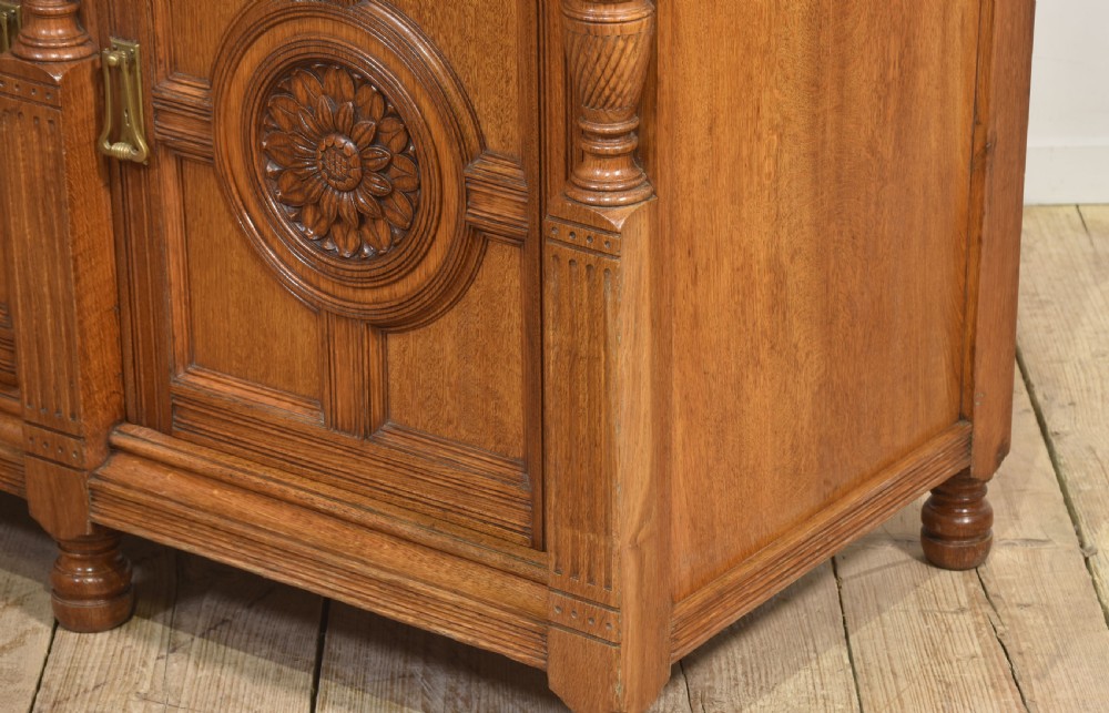 A carved oak two-door sideboard featuring two drawers with brass handles, central rosette carvings on the cupboard doors, and turned columns. View XV