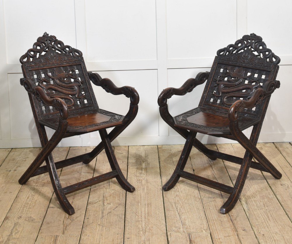 A pair of 19th-century Chinese folding hardwood armchairs featuring intricate dragon carvings on the backrests and serpentine arms supported by X-frame legs.