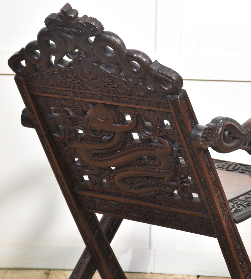A pair of 19th-century Chinese folding hardwood armchairs featuring intricate dragon carvings on the backrests and serpentine arms supported by X-frame legs. View X