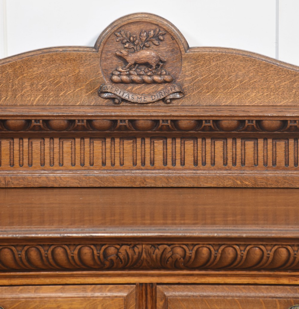 A carved oak serving table featuring a raised gallery back with a crest, two drawers with brass ring handles, and two open lower shelves supported by fluted turned legs. View III