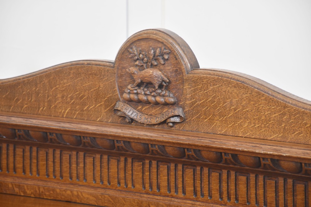 A carved oak serving table featuring a raised gallery back with a crest, two drawers with brass ring handles, and two open lower shelves supported by fluted turned legs. View XII