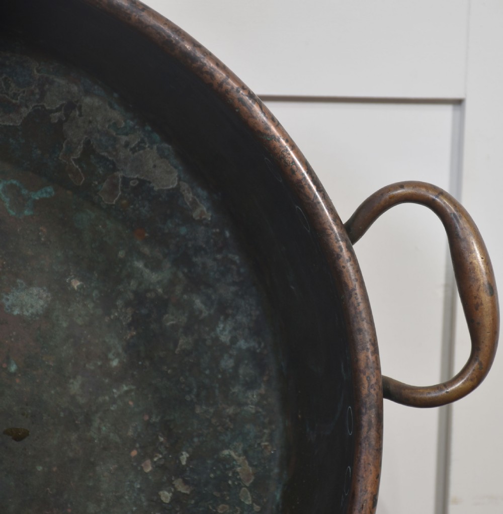 A large, wide, round 19th-century copper preserve pan featuring a rolled rim and two riveted loop handles. View V