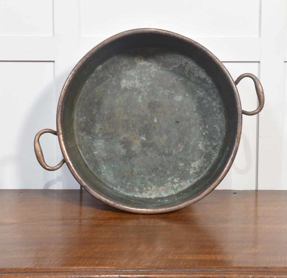 A large, wide, round 19th-century copper preserve pan featuring a rolled rim and two riveted loop handles. View VI