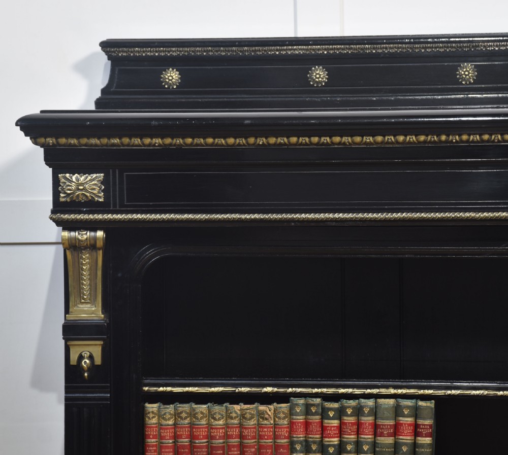 A large black ebonised open bookcase featuring four open shelves decorated with ornate brass mounts and a raised gallery top. View VI