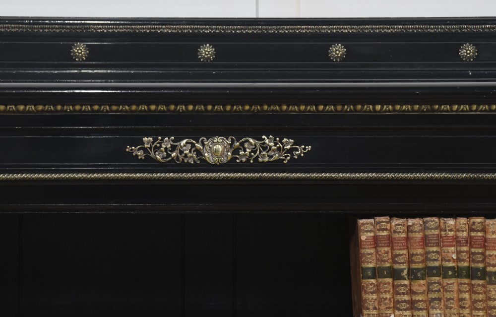 A large black ebonised open bookcase featuring four open shelves decorated with ornate brass mounts and a raised gallery top. View VII