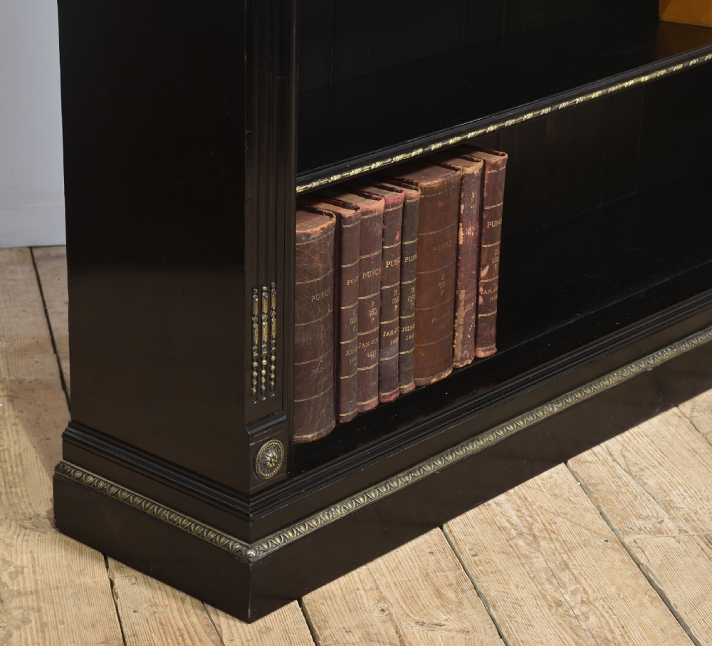 A large black ebonised open bookcase featuring four open shelves decorated with ornate brass mounts and a raised gallery top. View X