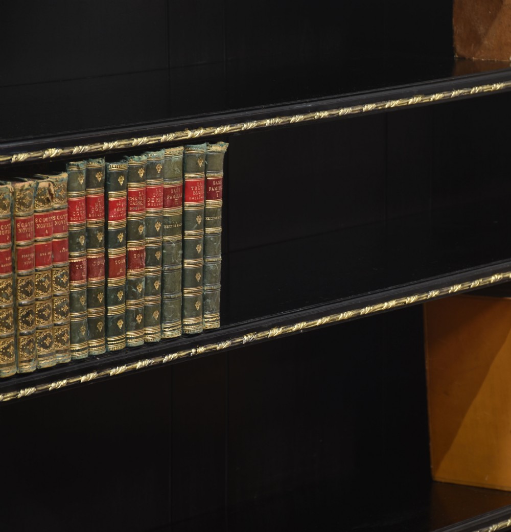 A large black ebonised open bookcase featuring four open shelves decorated with ornate brass mounts and a raised gallery top. View XII