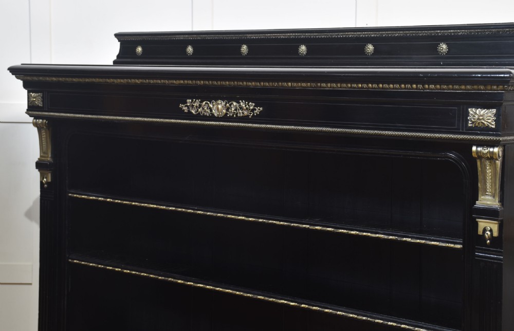 A large black ebonised open bookcase featuring four open shelves decorated with ornate brass mounts and a raised gallery top. View XV