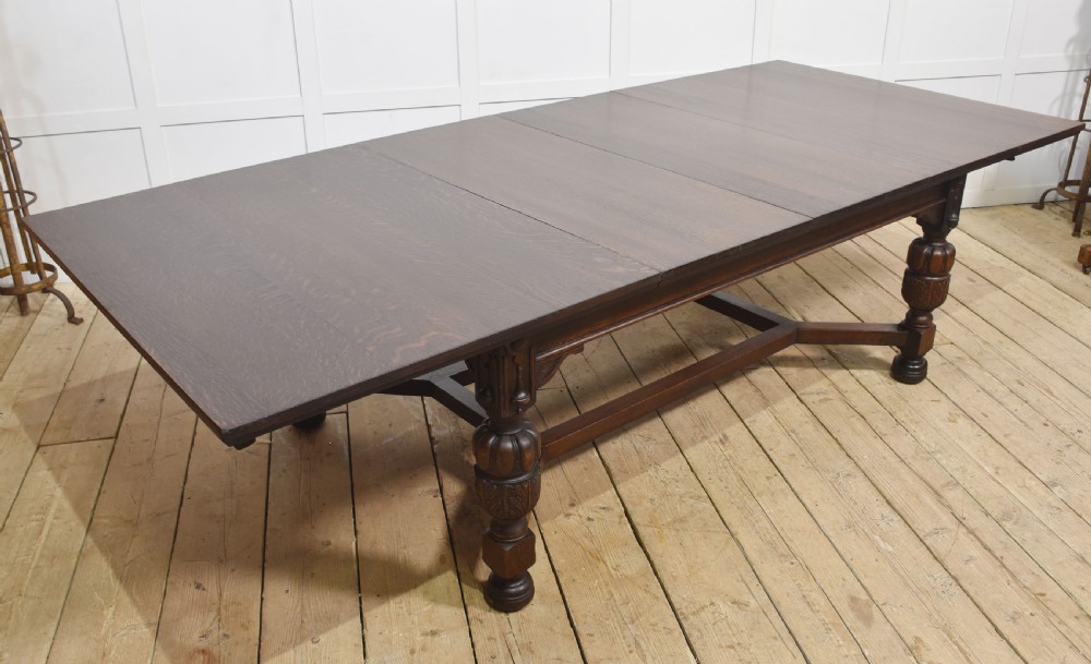 A dark oak extending dining table with carved bulbous legs and an H-stretcher base.