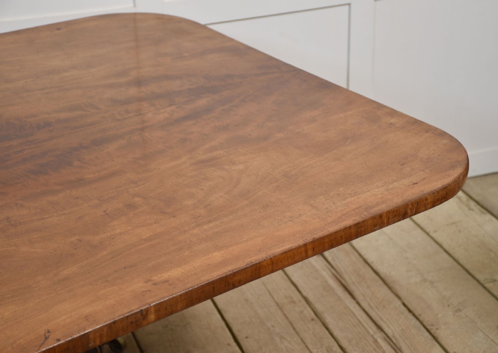 A Regency mahogany tilt-top breakfast table featuring a rectangular top with rounded corners, supported by a turned central pedestal and four splayed legs with brass paw castors. View III