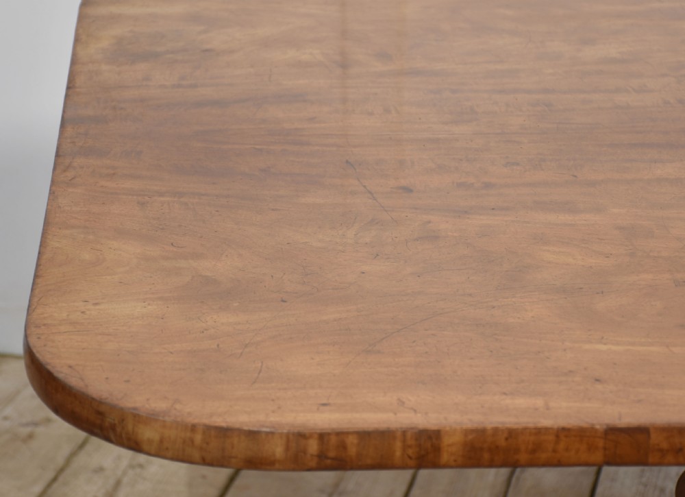 A Regency mahogany tilt-top breakfast table featuring a rectangular top with rounded corners, supported by a turned central pedestal and four splayed legs with brass paw castors. View V