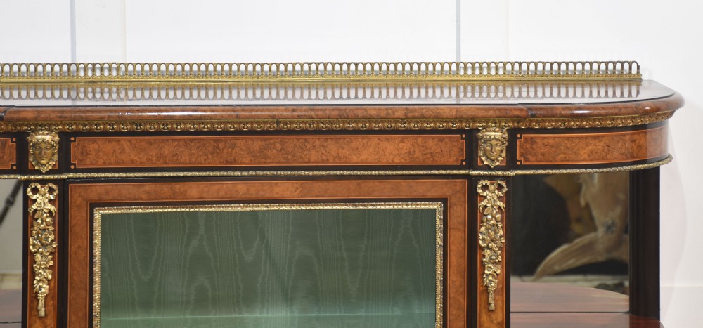 A 19th-century burr walnut credenza featuring a central glass door flanked by open curved shelves with mirrored backs and gilt-brass mounts. View V