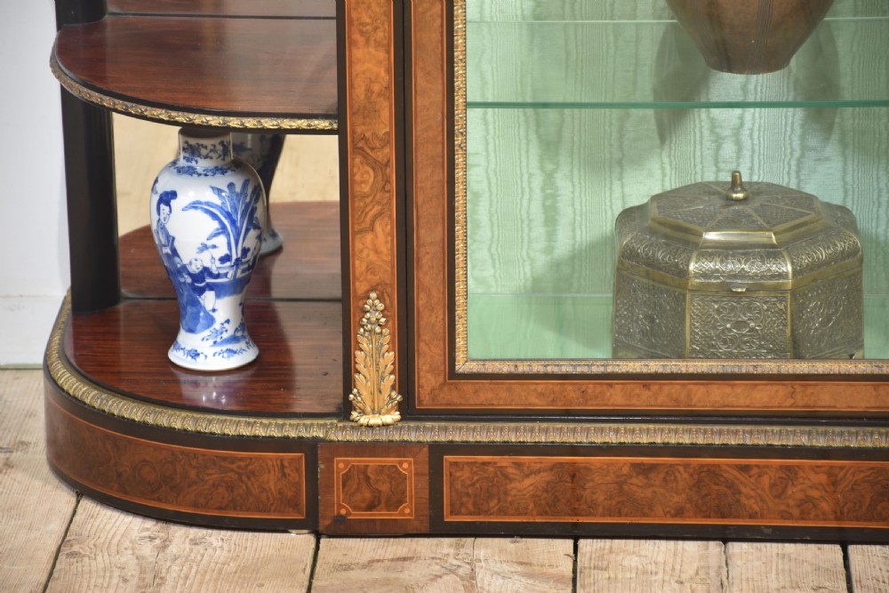 A 19th-century burr walnut credenza featuring a central glass door flanked by open curved shelves with mirrored backs and gilt-brass mounts. View VI