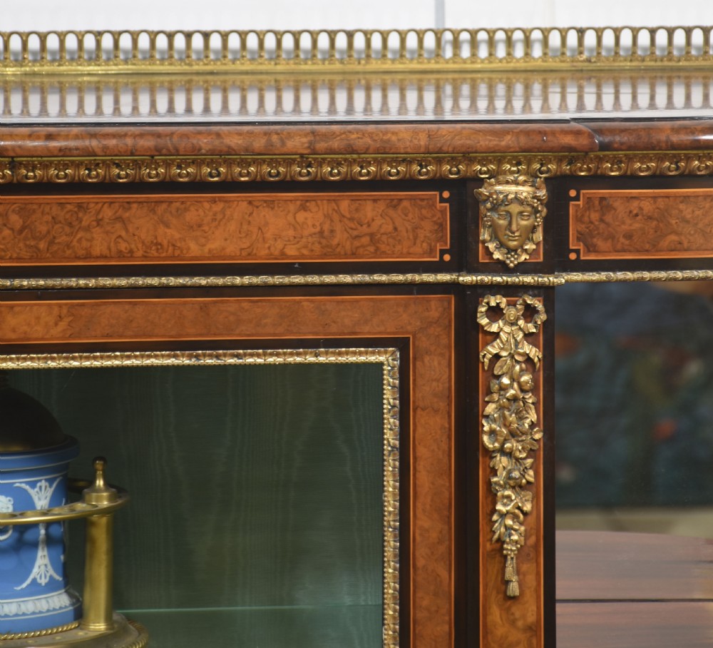 A 19th-century burr walnut credenza featuring a central glass door flanked by open curved shelves with mirrored backs and gilt-brass mounts. View VII