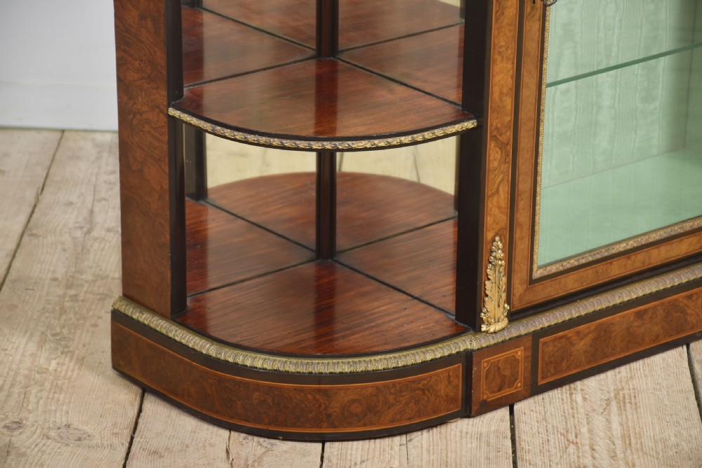 A 19th-century burr walnut credenza featuring a central glass door flanked by open curved shelves with mirrored backs and gilt-brass mounts. View X