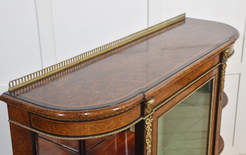 A 19th-century burr walnut credenza featuring a central glass door flanked by open curved shelves with mirrored backs and gilt-brass mounts. View XII