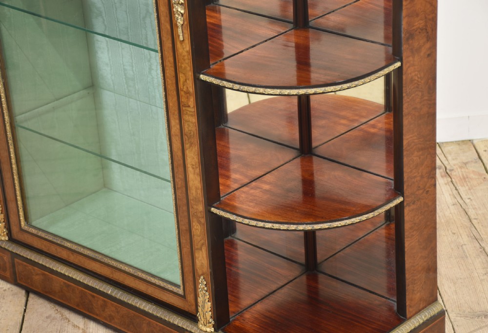 A 19th-century burr walnut credenza featuring a central glass door flanked by open curved shelves with mirrored backs and gilt-brass mounts. View XV