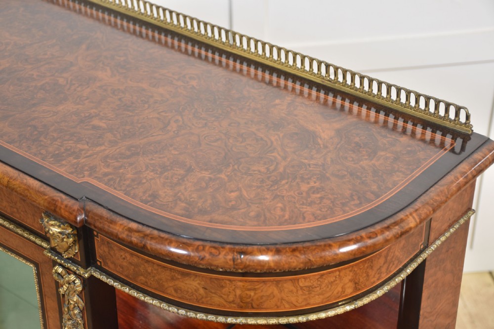 A 19th-century burr walnut credenza featuring a central glass door flanked by open curved shelves with mirrored backs and gilt-brass mounts. View XVI