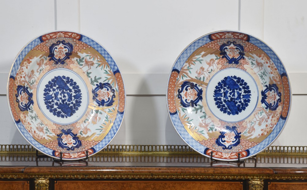 A pair of round Japanese Imari porcelain plates decorated with hand-painted cobalt blue, rust red, and gilded floral motifs.