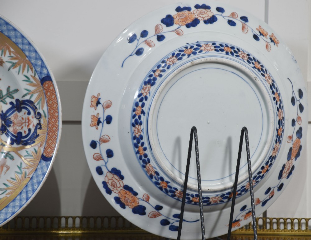 A pair of round Japanese Imari porcelain plates decorated with hand-painted cobalt blue, rust red, and gilded floral motifs. View X