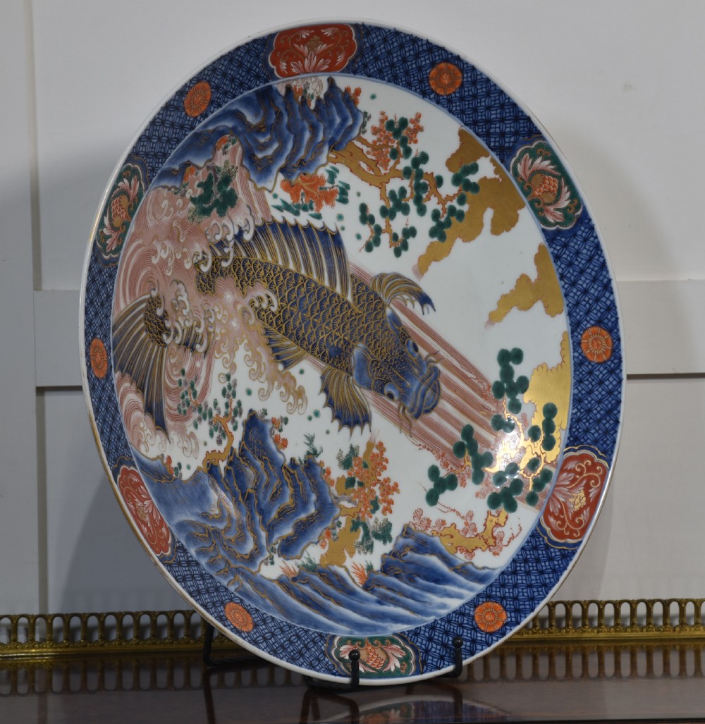 A circular Japanese Imari porcelain charger decorated with a blue and gold carp leaping up a waterfall amidst pine trees and geometric border motifs. View II