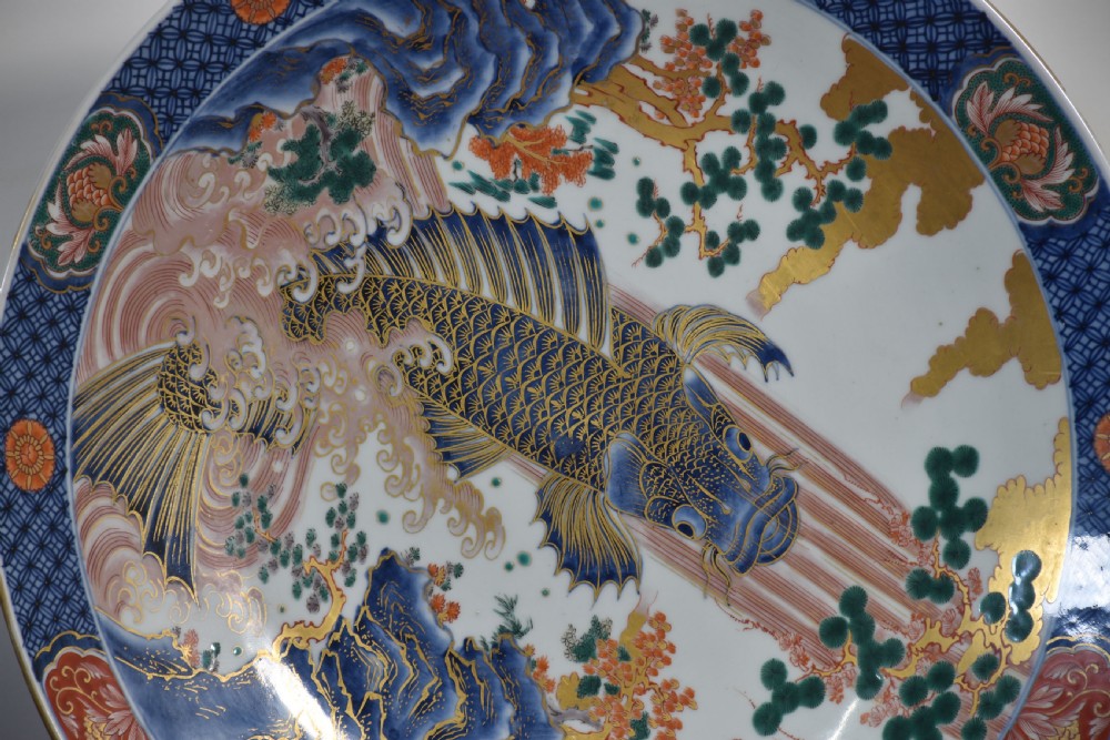 A circular Japanese Imari porcelain charger decorated with a blue and gold carp leaping up a waterfall amidst pine trees and geometric border motifs. View III