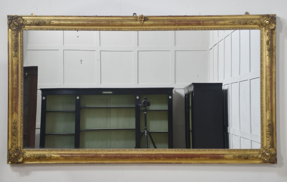 A large rectangular 19th-century wall mirror with a carved giltwood frame featuring ornate floral corner spandrels and moulded edges. View VI