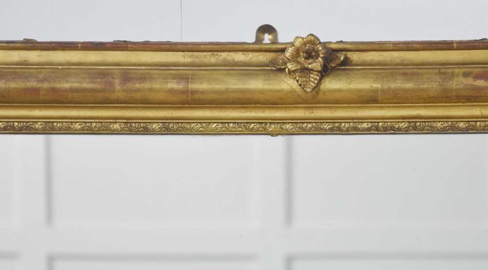 A large rectangular 19th-century wall mirror with a carved giltwood frame featuring ornate floral corner spandrels and moulded edges. View X