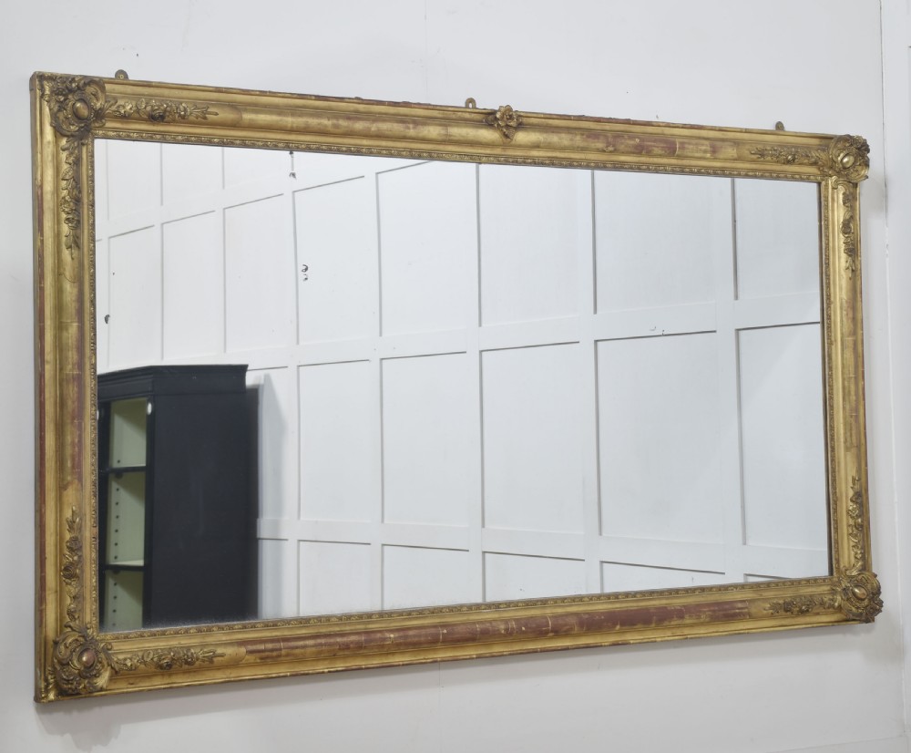 A large rectangular 19th-century wall mirror with a carved giltwood frame featuring ornate floral corner spandrels and moulded edges. View XII