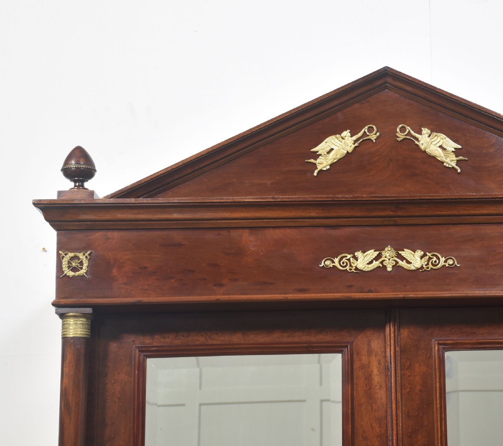 An Empire style mahogany wardrobe featuring twin mirrored doors, a classical pediment cornice, brass lion-ring drawer pulls, and gilt bronze mounts. View III