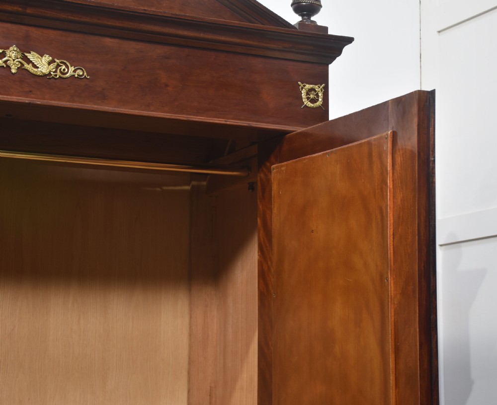 An Empire style mahogany wardrobe featuring twin mirrored doors, a classical pediment cornice, brass lion-ring drawer pulls, and gilt bronze mounts. View IX