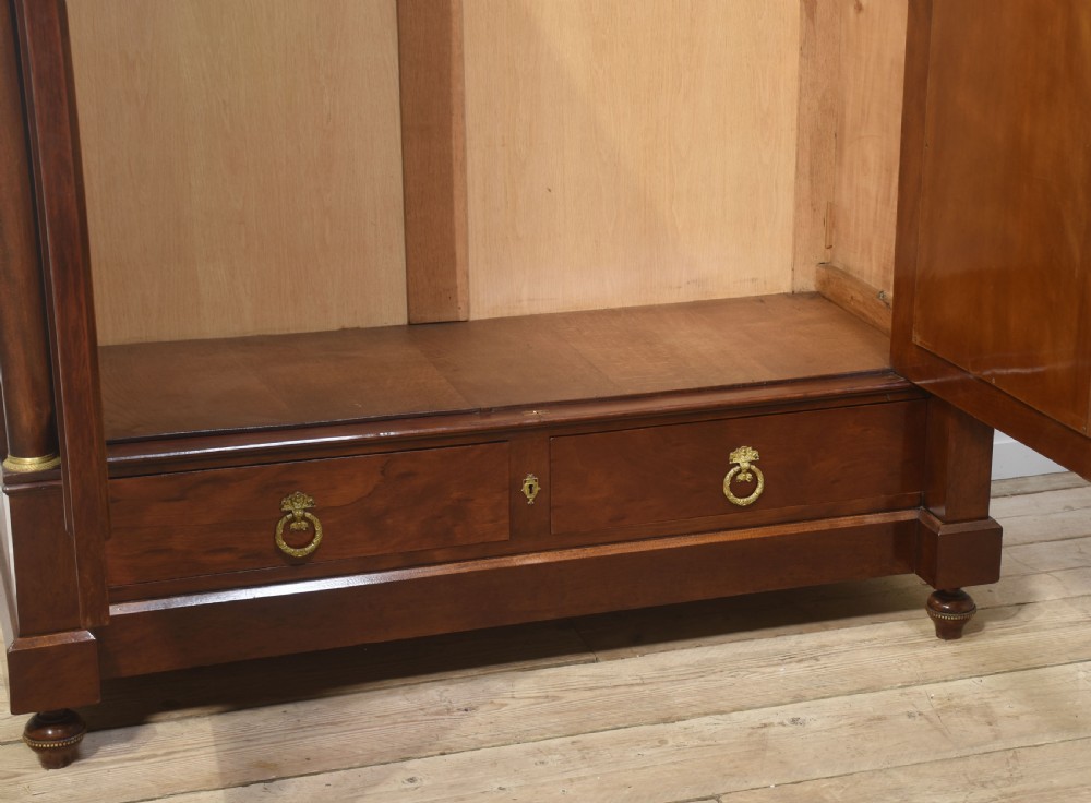 An Empire style mahogany wardrobe featuring twin mirrored doors, a classical pediment cornice, brass lion-ring drawer pulls, and gilt bronze mounts. View X