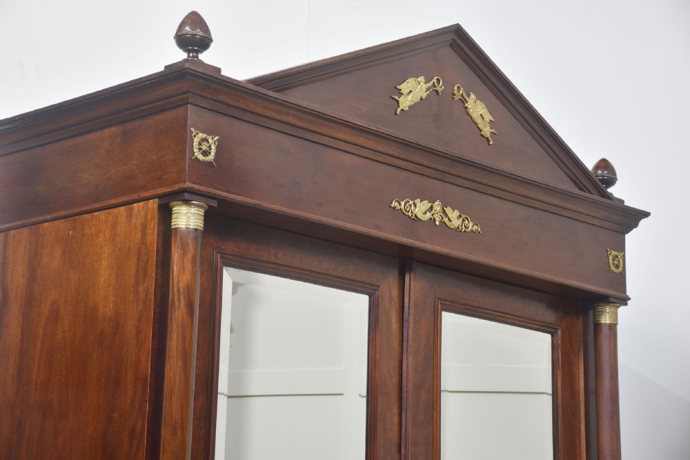 An Empire style mahogany wardrobe featuring twin mirrored doors, a classical pediment cornice, brass lion-ring drawer pulls, and gilt bronze mounts. View XIV