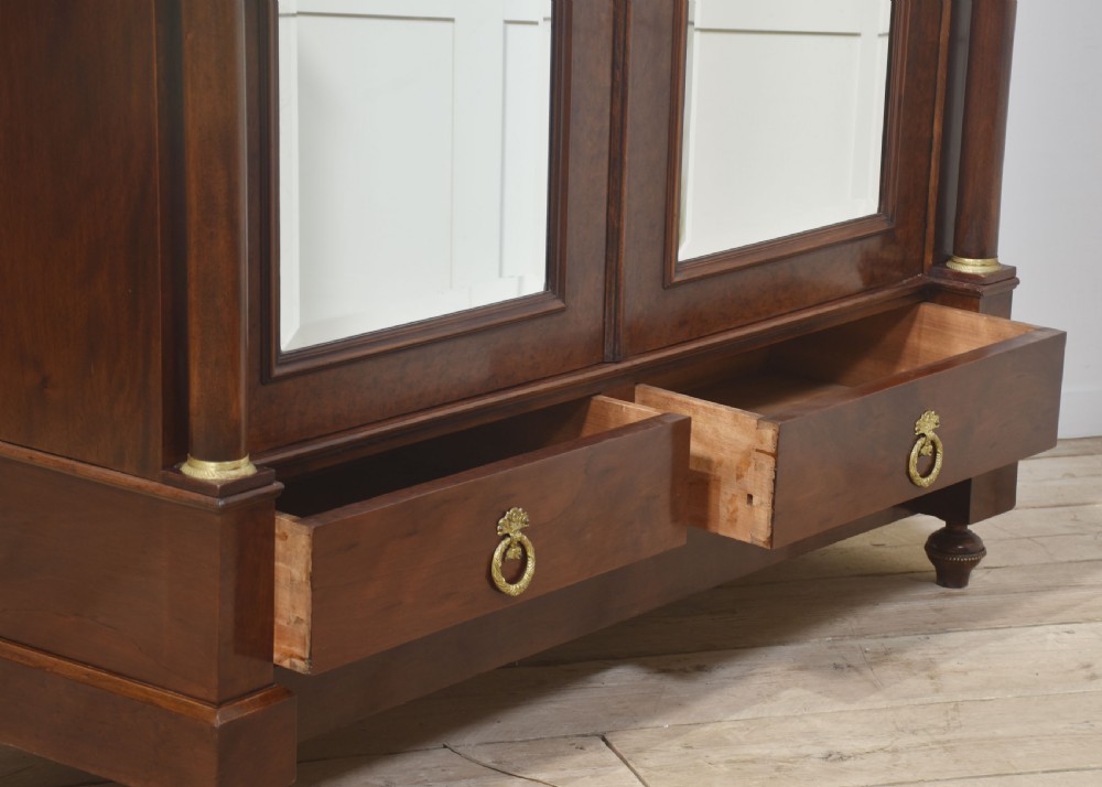 An Empire style mahogany wardrobe featuring twin mirrored doors, a classical pediment cornice, brass lion-ring drawer pulls, and gilt bronze mounts. View XVI