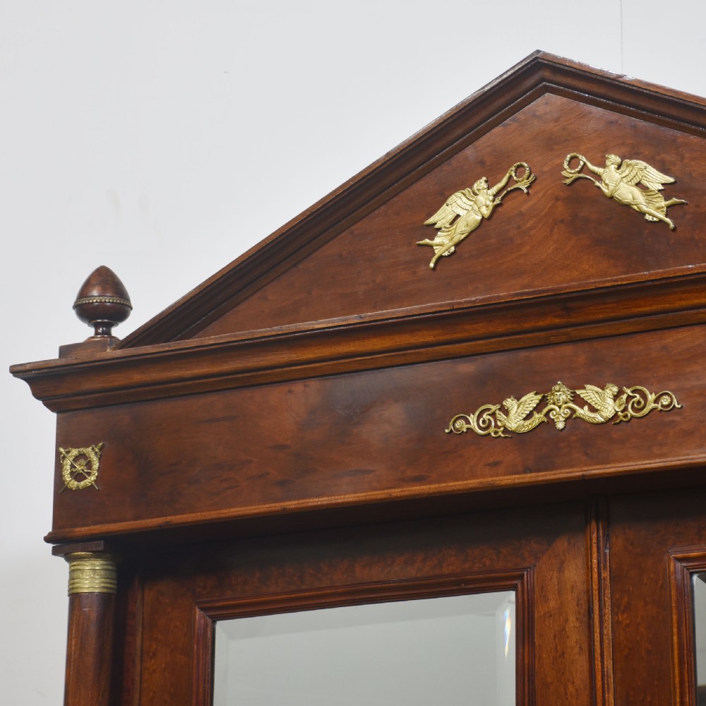 An Empire style mahogany wardrobe featuring twin mirrored doors, a classical pediment cornice, brass lion-ring drawer pulls, and gilt bronze mounts. View XIX
