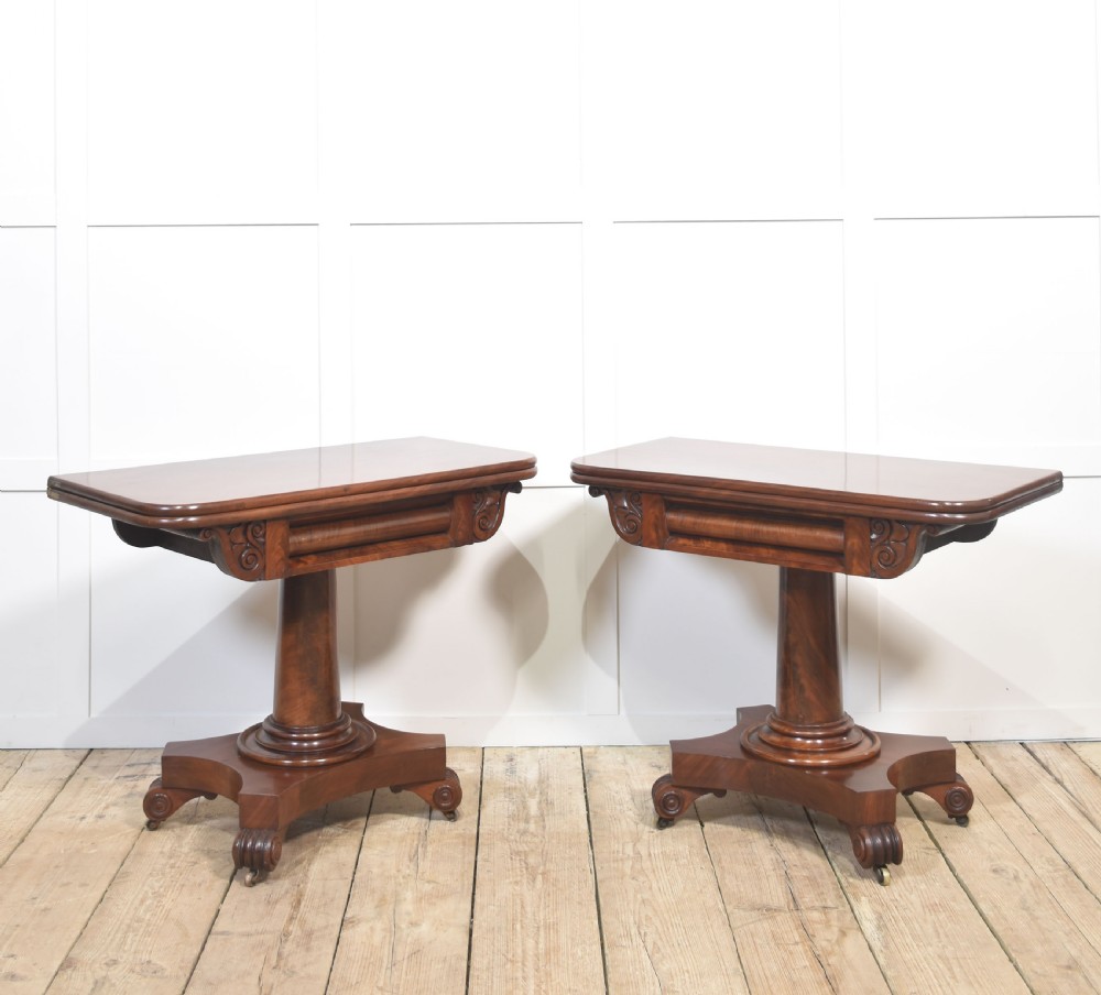 A pair of Regency mahogany fold-top tea tables resting on central cylindrical pedestals with quadruped scroll-foot bases.