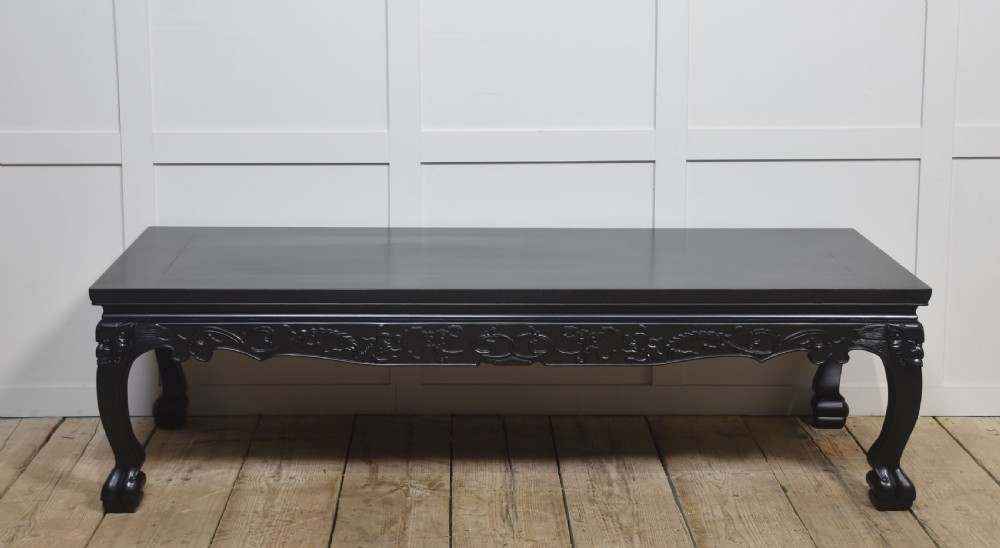 A low rectangular ebonised black wood coffee table featuring intricately carved aprons and shaped cabriole legs.