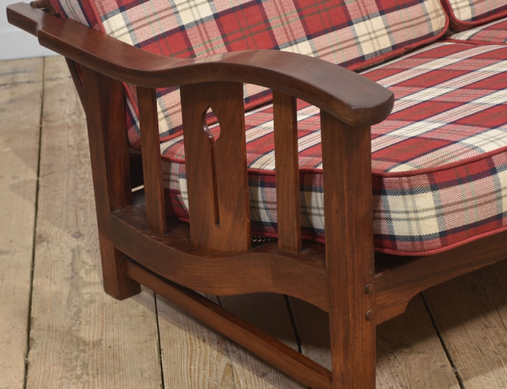 An Arts and Crafts solid walnut two-seater settee with red and cream tartan plaid upholstered cushions. View II