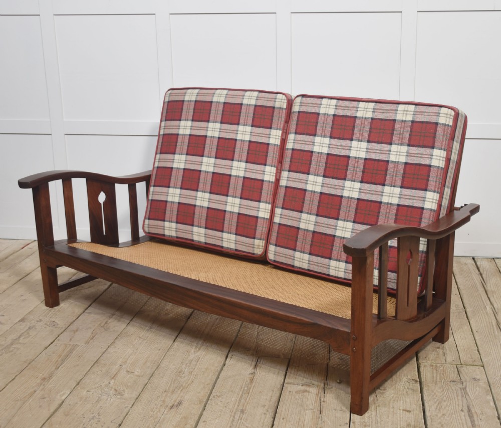 An Arts and Crafts solid walnut two-seater settee with red and cream tartan plaid upholstered cushions. View III