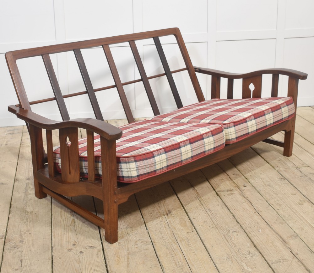 An Arts and Crafts solid walnut two-seater settee with red and cream tartan plaid upholstered cushions. View IV