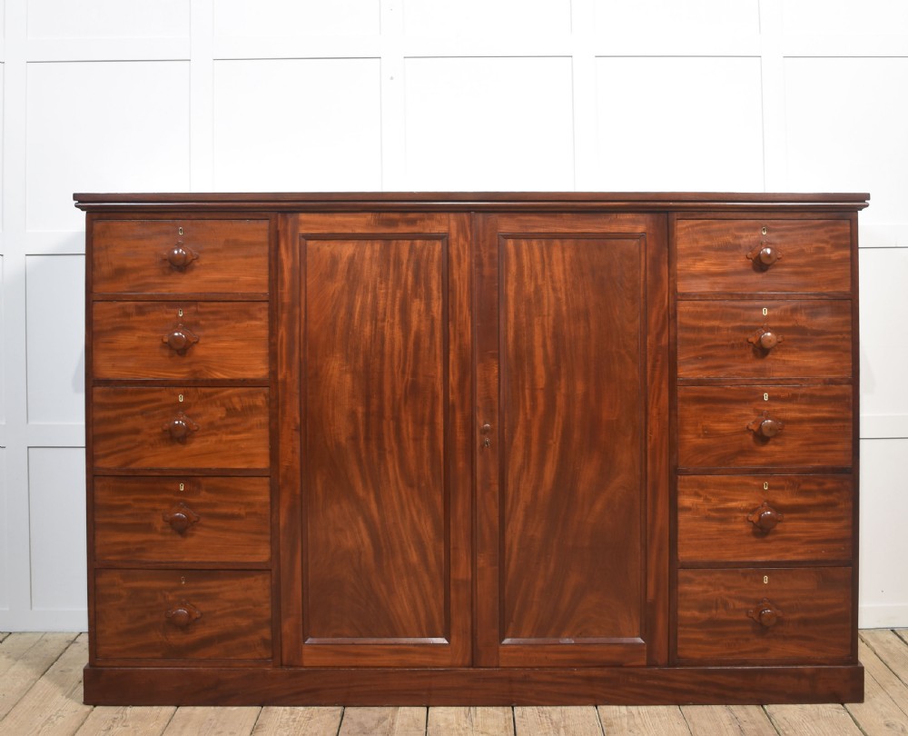 A 19th-century low mahogany linen press with a central double-door cupboard flanked by ten drawers with turned wooden knobs.